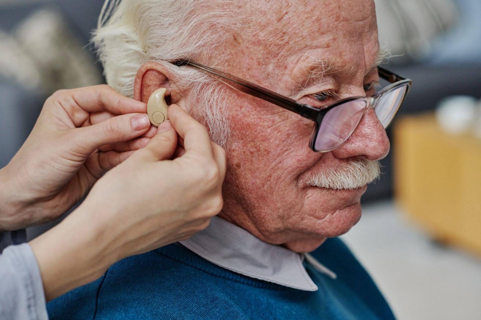 Audiologist fitting a hearing aid on a senior man
